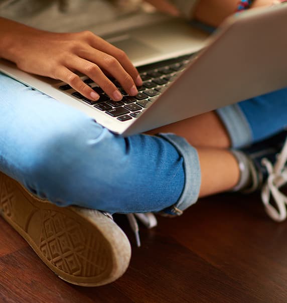 Teenager sat cross legged with laptop on lap.