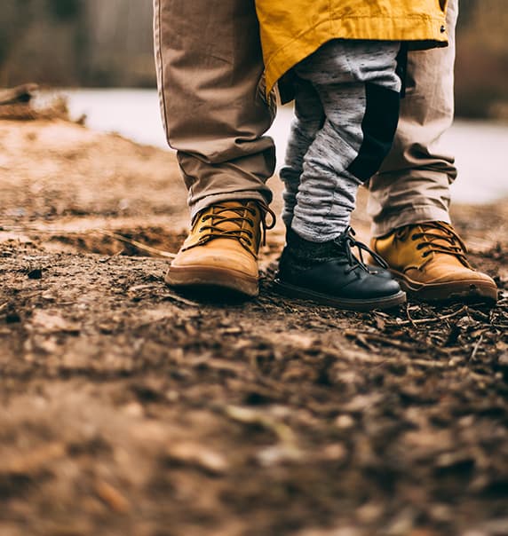 Father and child in boots walking along trail.