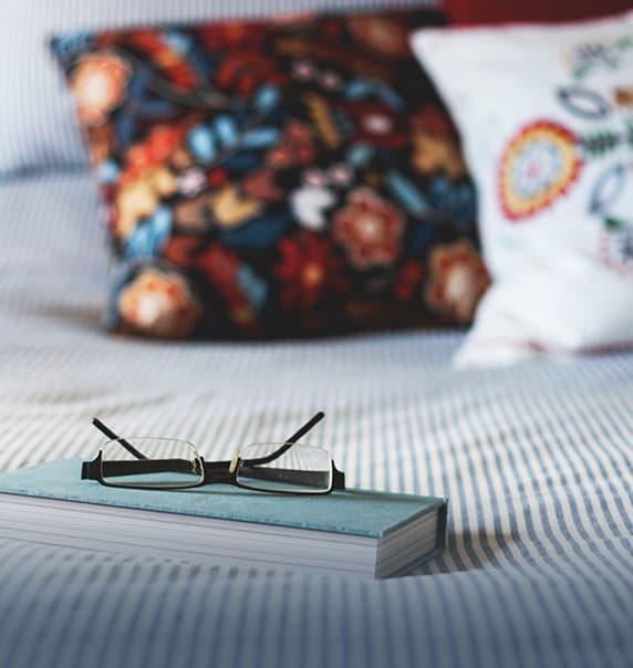 Notebook and glasses on a made bed.