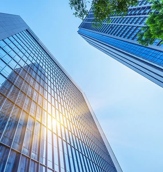 Tall glass buildings with tree from human perspective looking at sky.