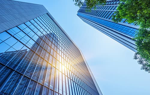 Tall glass buildings with tree from human perspective looking at sky.
