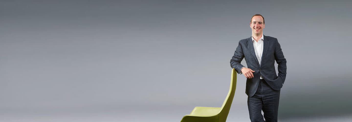 Podcast host and Partner, Adam Walford, leaning on a chair and smiling down the camera. 