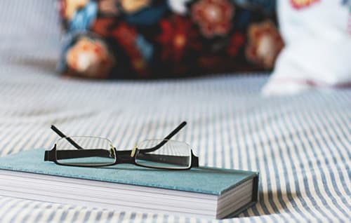 Notebook on bed with glasses on top.