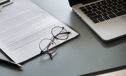 Laptop, Glasses and document on desk.
