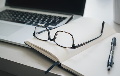 Desk with laptop, notebook, glasses and pen